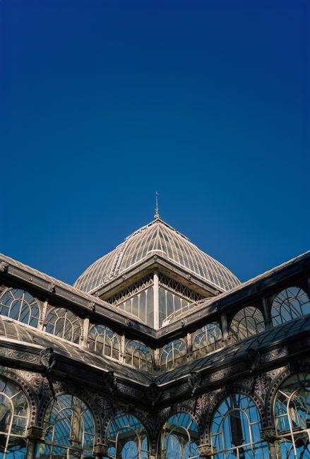 A glass conservatory with ornate yellow and gold decorative features, large arched windows, and intricate painted detailing along the lower sections. The structure is partially illuminated by sunlight